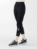 A pair of high-waisted black capri leggings with mesh panels, featuring a logo on the left thigh, paired with sneakers.